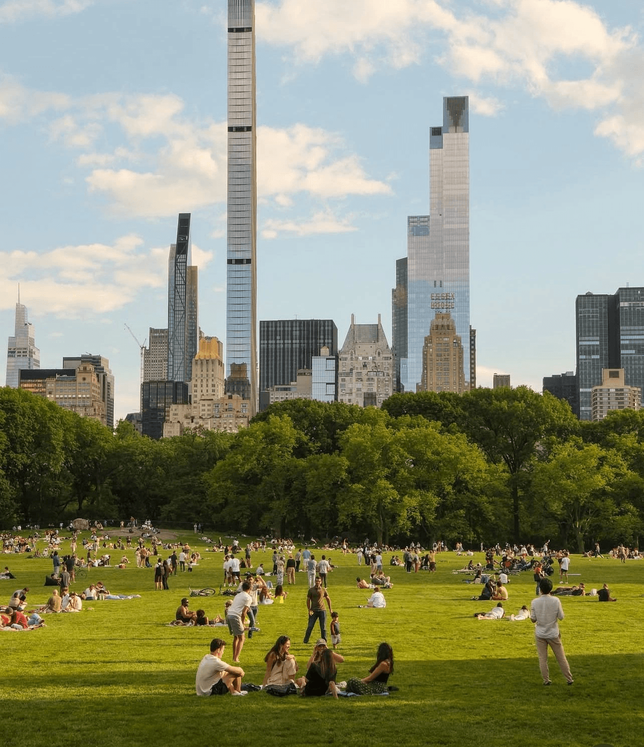 People relaxing on the lawn in Central Park with the Manhattan skyline beyond